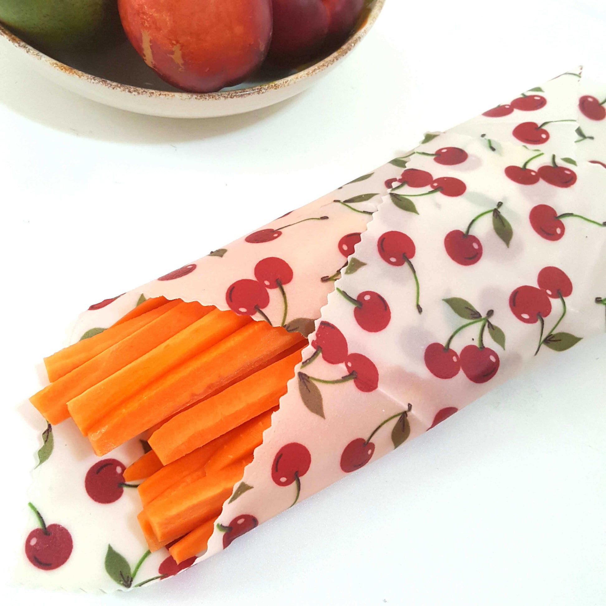 Reusable Beeswax Food Wraps 100% Hand Made in the UK by Honey Bee Good. Planet-Kind single large beeswax wrap in Cherries pattern as flatlay with carrots