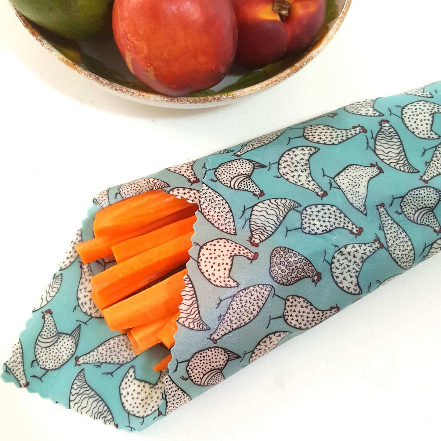 Reusable Beeswax Food Wraps 100% Hand Made in the UK by Honey Bee Good. Planet-Kind single large beeswax wrap in Happy Hens pattern as flatlay with carrots