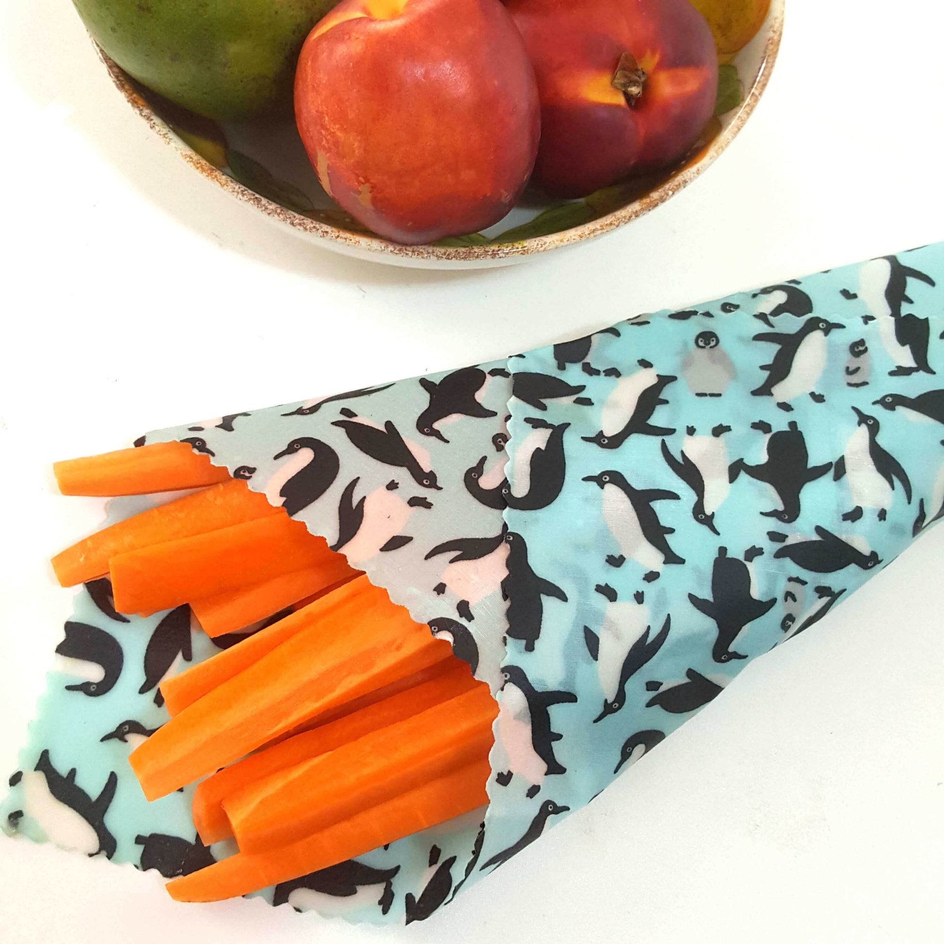 Reusable Beeswax Food Wraps 100% Hand Made in the UK by Honey Bee Good. Planet-Kind single large beeswax wrap in Penguins pattern as flatlay with carrots