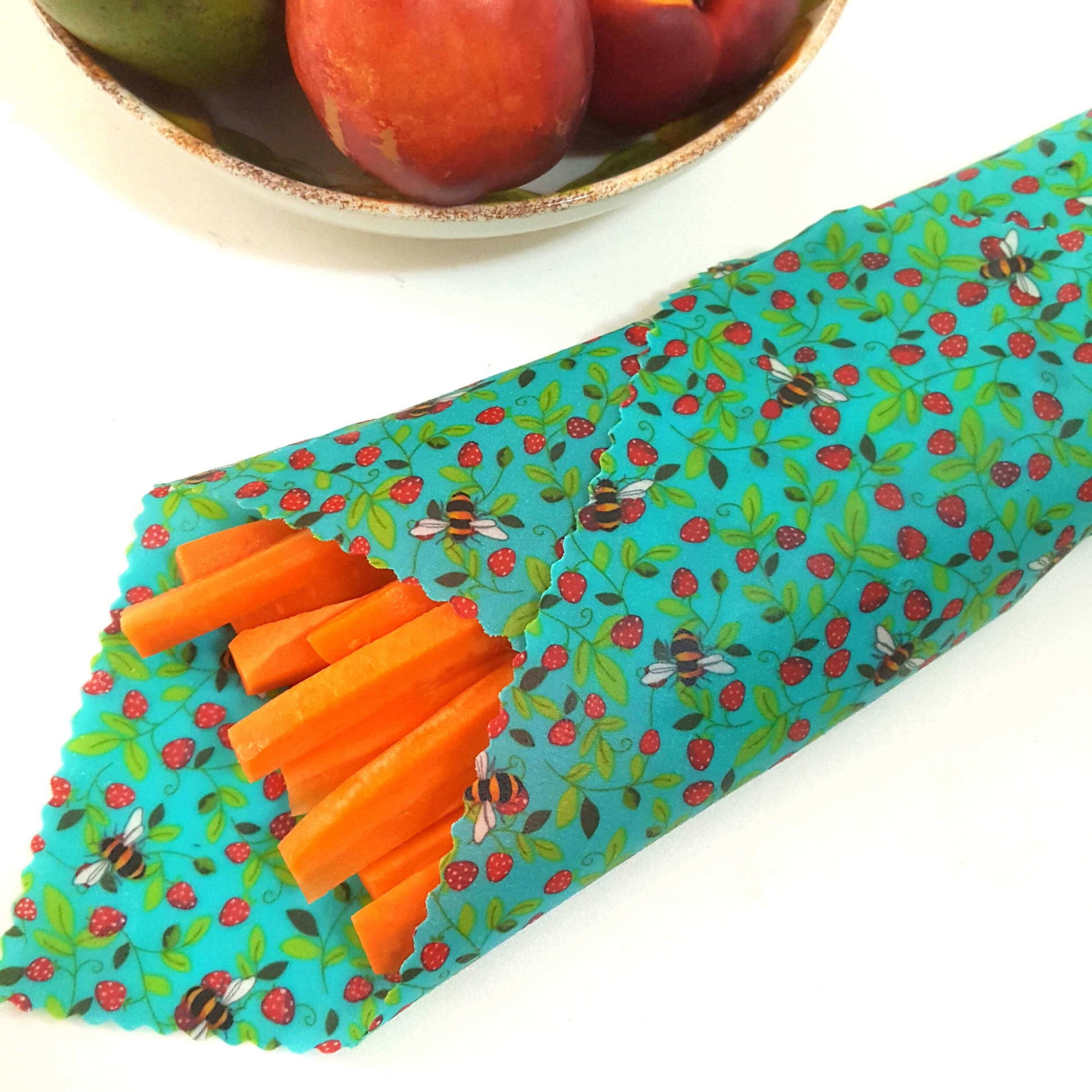 Reusable Beeswax Food Wraps 100% Hand Made in the UK by Honey Bee Good. Planet-Kind single large beeswax wrap in Strawberry Bees pattern as flatlay with carrots